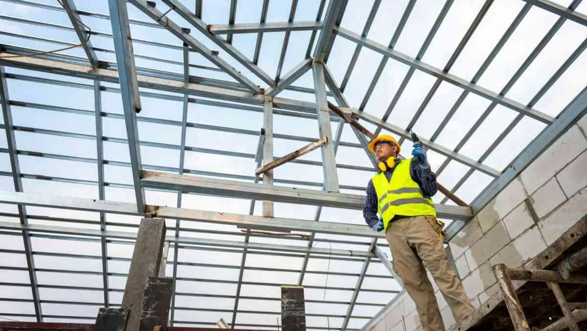 A construction worker erecting steel roof trusses of a residential building.