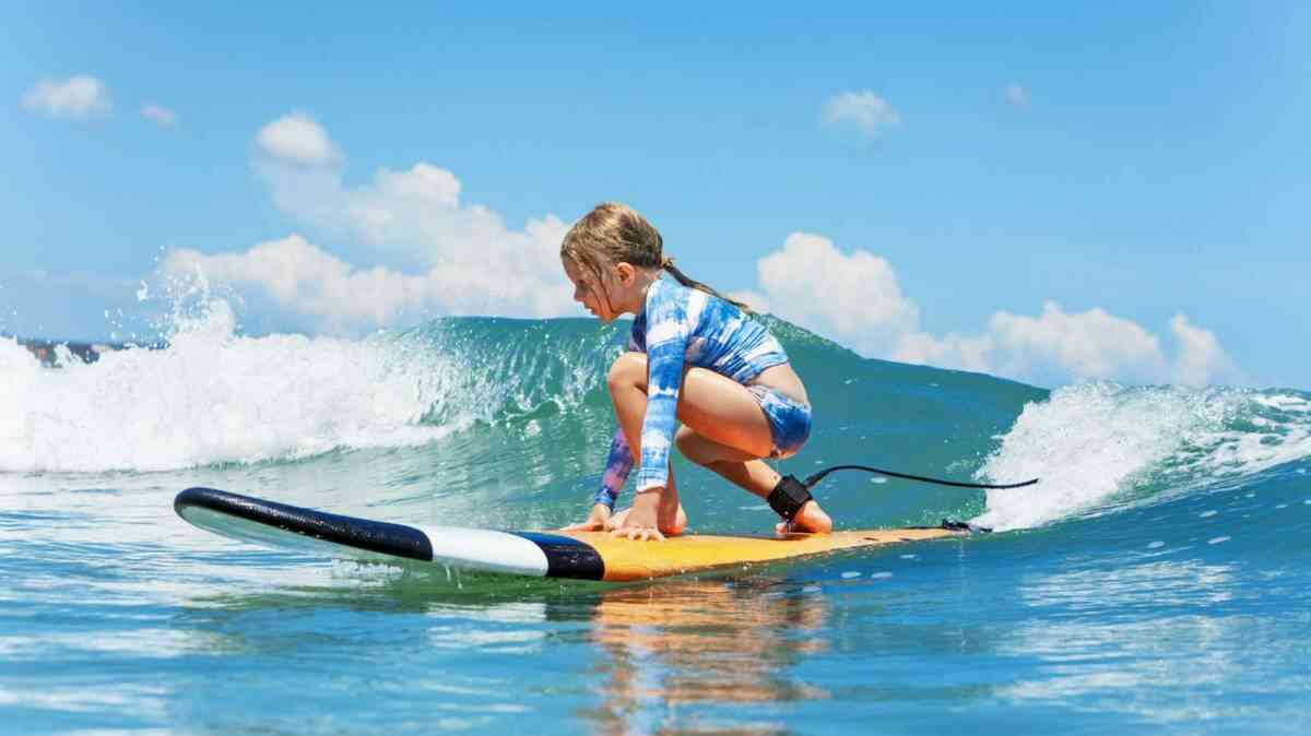 A kid surfer wearing protective surf gear whilst riding the waves.